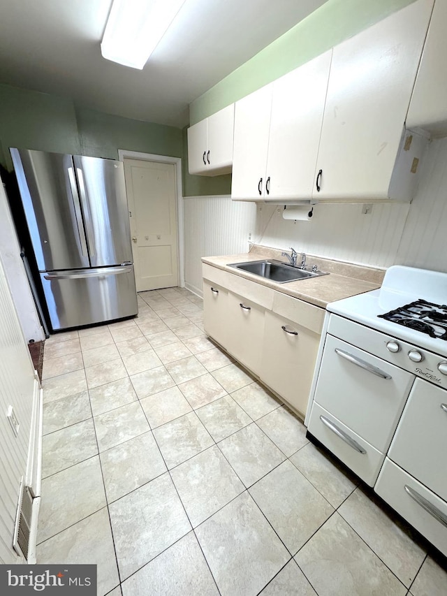 kitchen with stainless steel refrigerator, white cabinetry, sink, white range, and light tile patterned floors