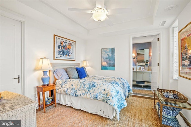 carpeted bedroom with ensuite bathroom, ceiling fan, and a tray ceiling