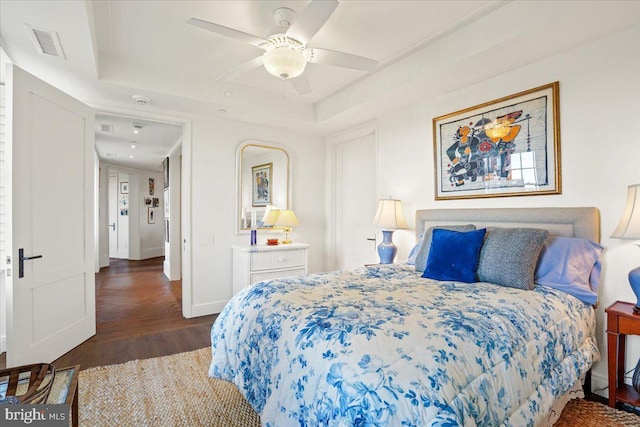 bedroom with dark hardwood / wood-style flooring, ceiling fan, and a tray ceiling