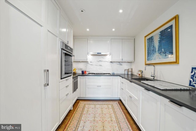 kitchen with hardwood / wood-style floors, backsplash, white cabinets, appliances with stainless steel finishes, and sink