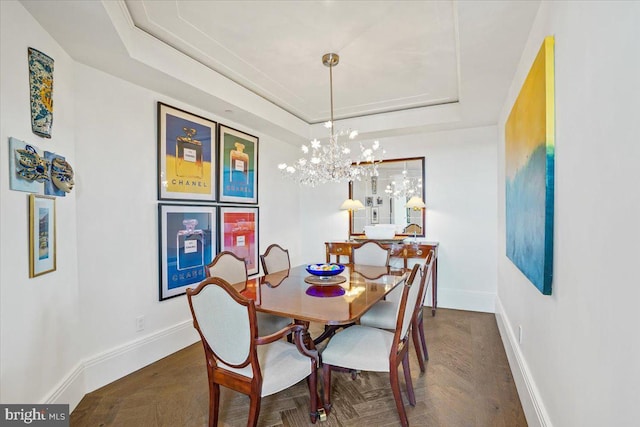 dining area with a raised ceiling, dark parquet flooring, and a notable chandelier