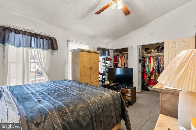 bedroom with lofted ceiling, light colored carpet, a textured ceiling, multiple closets, and ceiling fan