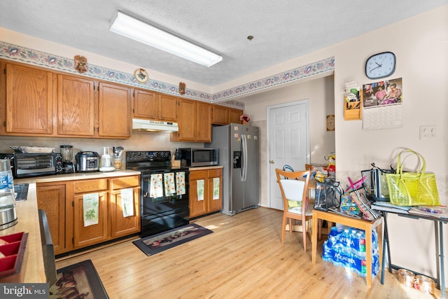 kitchen with light wood-type flooring, a textured ceiling, and appliances with stainless steel finishes