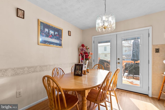 dining space featuring a chandelier, light hardwood / wood-style flooring, a textured ceiling, and french doors