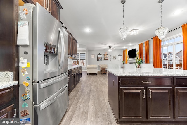 kitchen with stainless steel fridge with ice dispenser, light wood-type flooring, dark brown cabinets, pendant lighting, and ceiling fan with notable chandelier