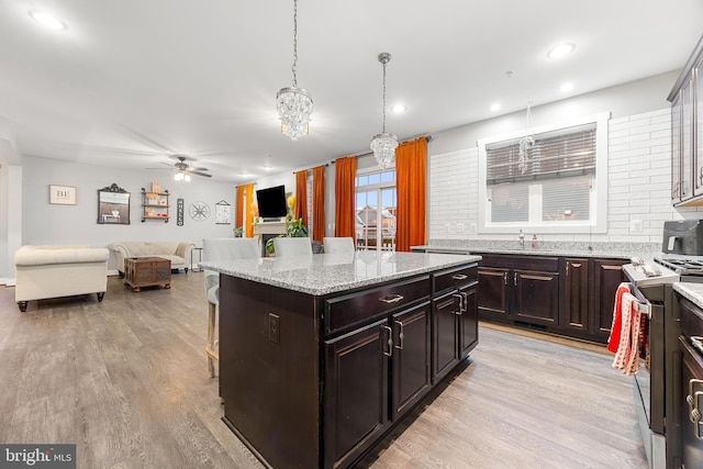 kitchen featuring a center island, decorative light fixtures, stainless steel stove, light wood-type flooring, and dark brown cabinets