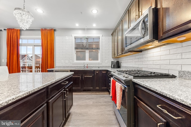 kitchen featuring light hardwood / wood-style floors, hanging light fixtures, stainless steel appliances, dark brown cabinets, and light stone counters