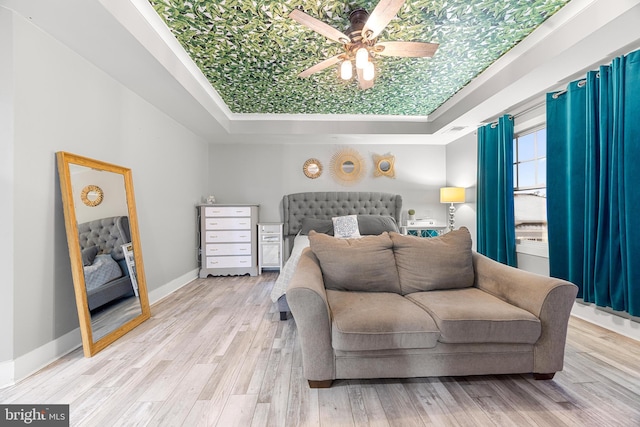 bedroom featuring ceiling fan, light hardwood / wood-style floors, a tray ceiling, and ornamental molding