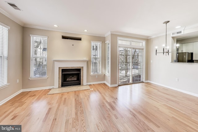 unfurnished living room featuring light hardwood / wood-style floors, ornamental molding, an inviting chandelier, and plenty of natural light