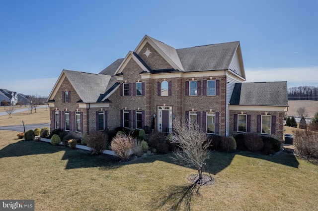 view of front of home featuring brick siding, a front yard, and a shingled roof