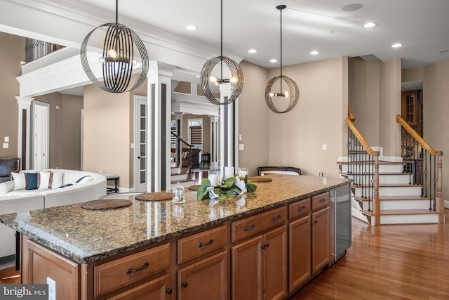 kitchen with wood finished floors, recessed lighting, dark stone counters, brown cabinetry, and decorative columns