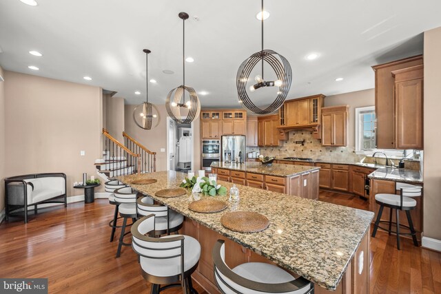 kitchen with backsplash, a large island with sink, dark wood-style floors, stainless steel appliances, and a sink