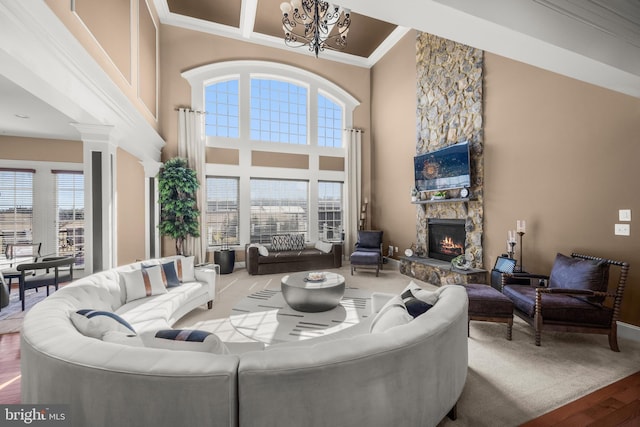 living area featuring a notable chandelier, a high ceiling, a stone fireplace, and ornamental molding