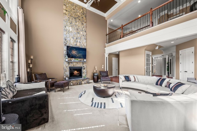 living area with crown molding, carpet, a fireplace, a high ceiling, and ornate columns