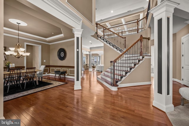 entrance foyer with a chandelier, stairs, ornamental molding, hardwood / wood-style flooring, and ornate columns