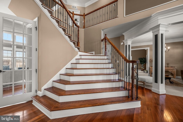 stairs featuring crown molding, baseboards, decorative columns, a high ceiling, and wood-type flooring