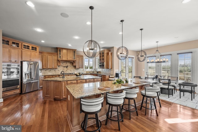 kitchen with backsplash, an island with sink, brown cabinets, and appliances with stainless steel finishes