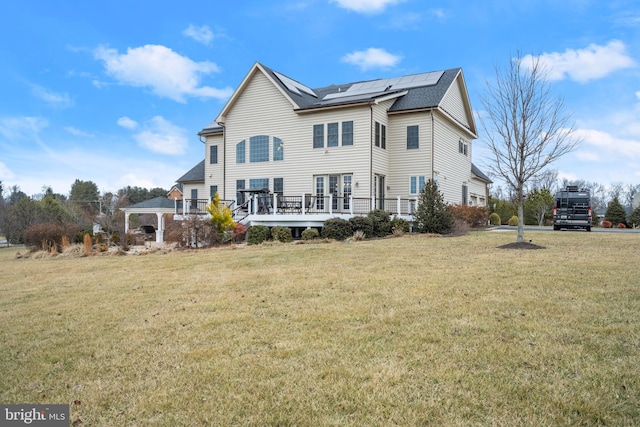 rear view of house with a gazebo, roof mounted solar panels, a wooden deck, and a yard