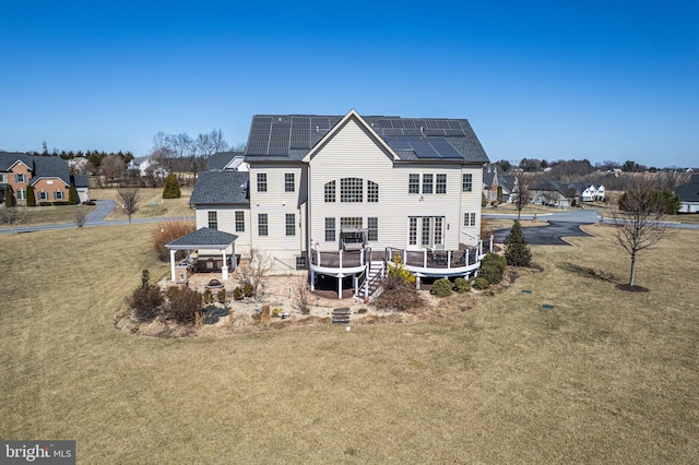 rear view of property with a gazebo, roof mounted solar panels, a lawn, and a wooden deck