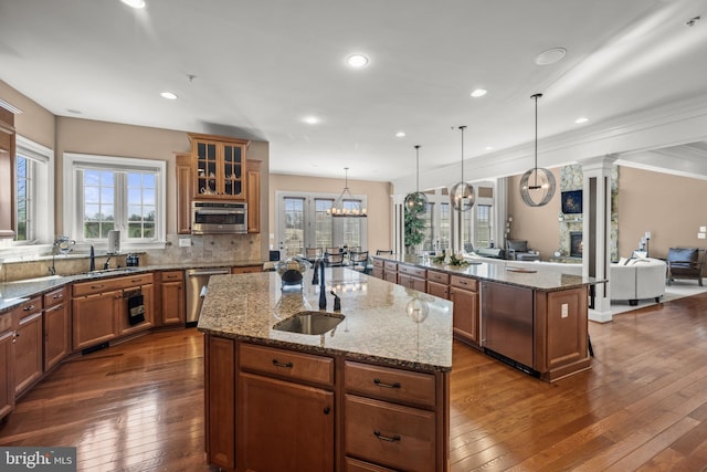 kitchen featuring brown cabinetry, a sink, an island with sink, and stainless steel dishwasher