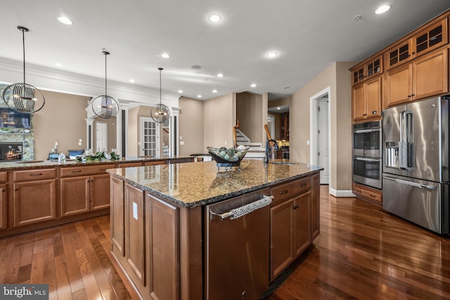 kitchen featuring dark wood finished floors, an island with sink, a fireplace, stainless steel appliances, and a sink