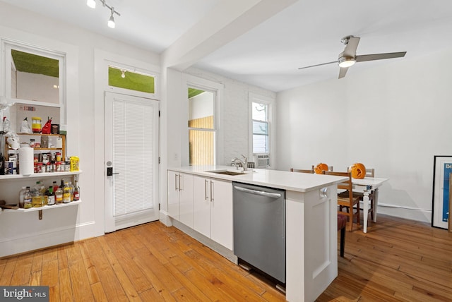 kitchen featuring kitchen peninsula, light wood-type flooring, stainless steel dishwasher, sink, and white cabinets