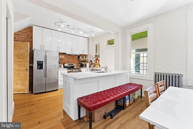 kitchen featuring brick wall, stainless steel appliances, light hardwood / wood-style flooring, radiator heating unit, and white cabinetry