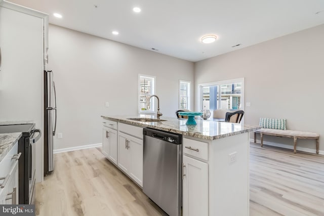 kitchen with appliances with stainless steel finishes, light stone counters, sink, white cabinets, and an island with sink