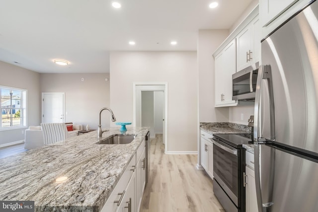 kitchen with white cabinets, appliances with stainless steel finishes, light stone counters, and sink