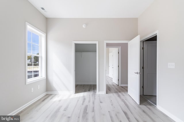 unfurnished bedroom featuring light wood-type flooring, a walk in closet, and a closet