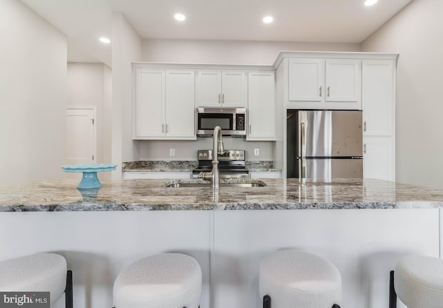 kitchen with appliances with stainless steel finishes, light stone counters, sink, white cabinetry, and a breakfast bar area