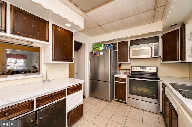 kitchen with appliances with stainless steel finishes, dark brown cabinets, ceiling fan, sink, and light tile patterned floors