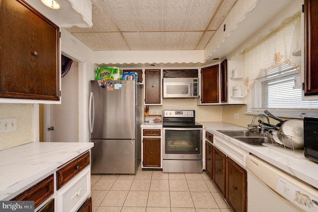 kitchen with light tile patterned flooring, appliances with stainless steel finishes, light stone countertops, and sink