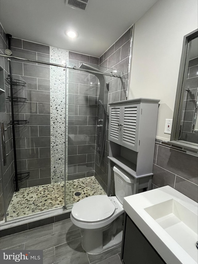 bathroom with vanity, toilet, tile walls, and a shower with shower door