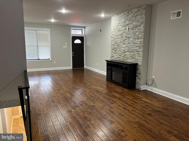 unfurnished living room featuring a stone fireplace and dark hardwood / wood-style flooring