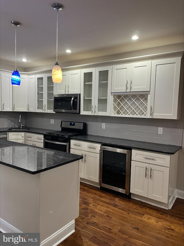 kitchen featuring dark wood-type flooring, white cabinets, hanging light fixtures, stainless steel appliances, and beverage cooler