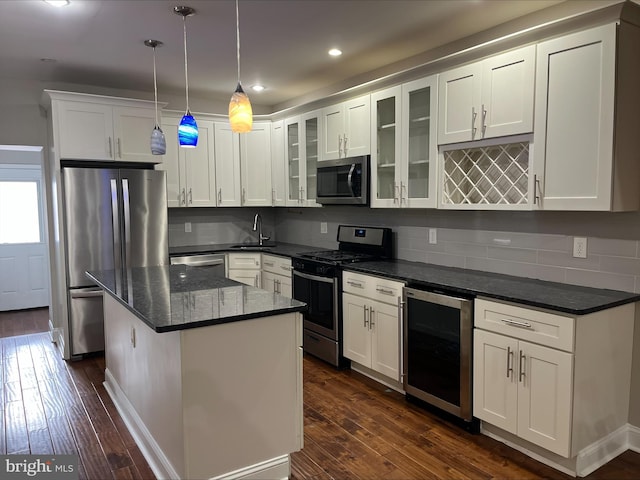 kitchen with appliances with stainless steel finishes, beverage cooler, dark wood-type flooring, a kitchen island, and hanging light fixtures