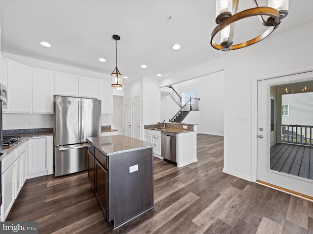 kitchen featuring dark stone countertops, hanging light fixtures, stainless steel appliances, white cabinets, and a kitchen island