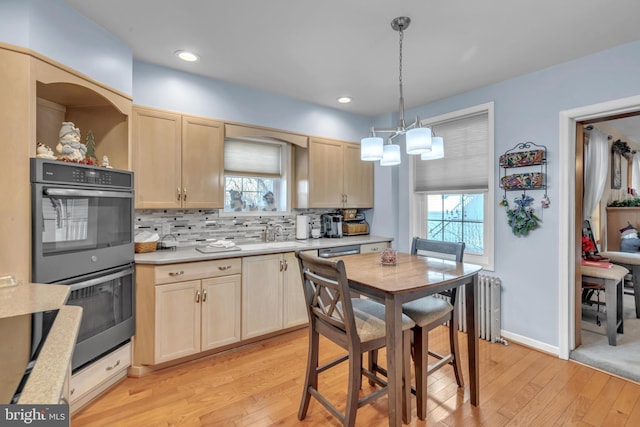 kitchen featuring radiator, light brown cabinetry, light hardwood / wood-style floors, hanging light fixtures, and multiple ovens