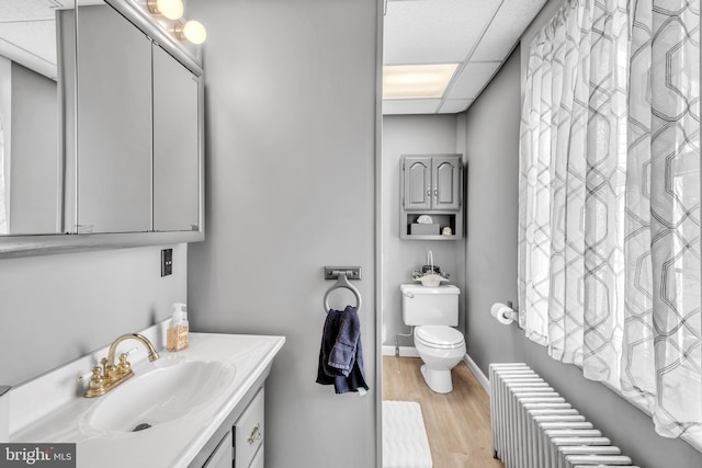 bathroom featuring toilet, vanity, hardwood / wood-style flooring, radiator, and a paneled ceiling