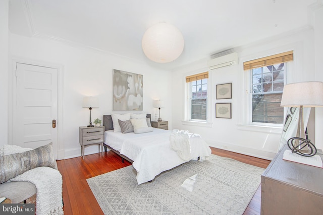 bedroom featuring ornamental molding, baseboards, wood-type flooring, and a wall mounted AC