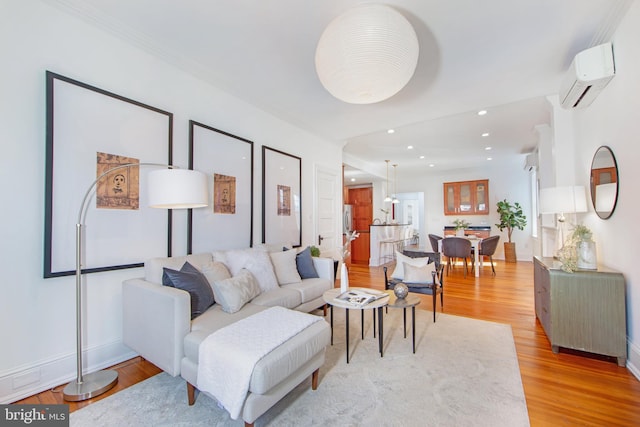 living room featuring light wood finished floors, crown molding, baseboards, a wall unit AC, and recessed lighting