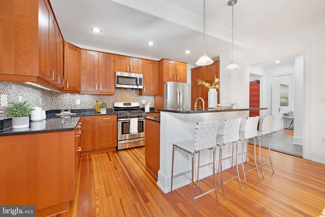 kitchen with a breakfast bar, light wood-style flooring, appliances with stainless steel finishes, dark countertops, and tasteful backsplash