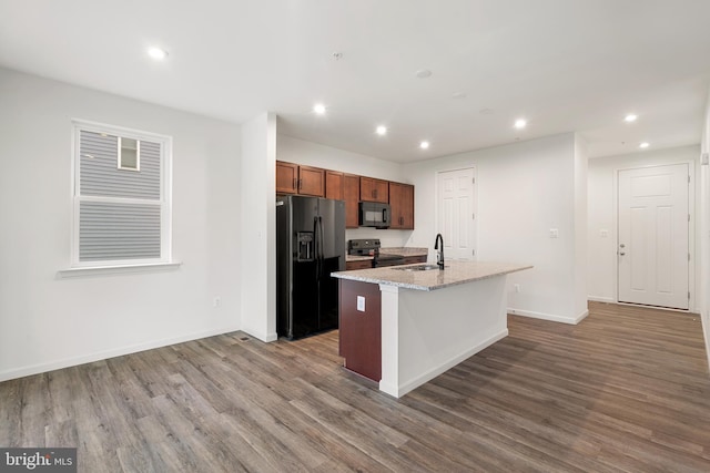 kitchen featuring light stone countertops, sink, an island with sink, black appliances, and hardwood / wood-style flooring