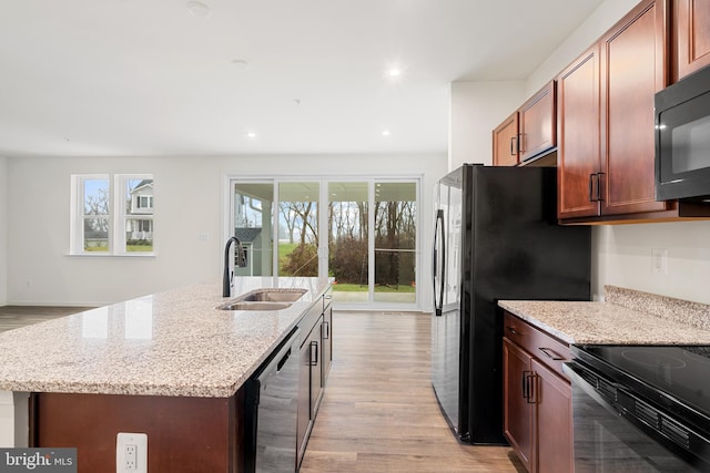 kitchen with a healthy amount of sunlight, light stone counters, a kitchen island with sink, and appliances with stainless steel finishes