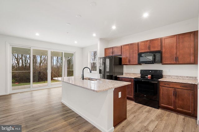 kitchen featuring light stone countertops, sink, black appliances, and a center island with sink