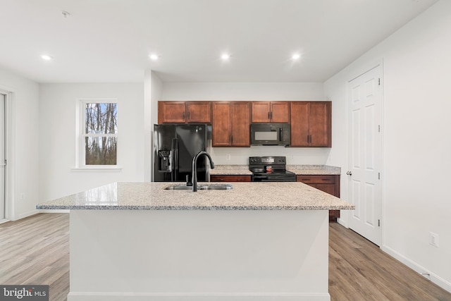 kitchen with black appliances, light hardwood / wood-style floors, sink, and an island with sink