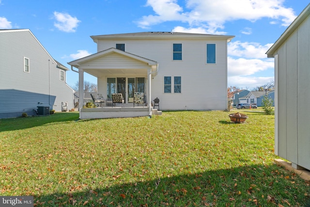 back of house with central air condition unit, a yard, and an outdoor fire pit