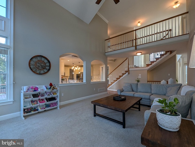 carpeted living room featuring ceiling fan with notable chandelier, a towering ceiling, and plenty of natural light