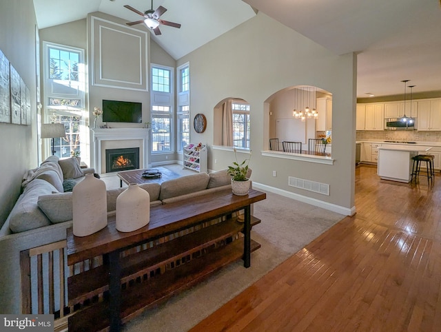 living room with light wood-type flooring, high vaulted ceiling, and ceiling fan with notable chandelier